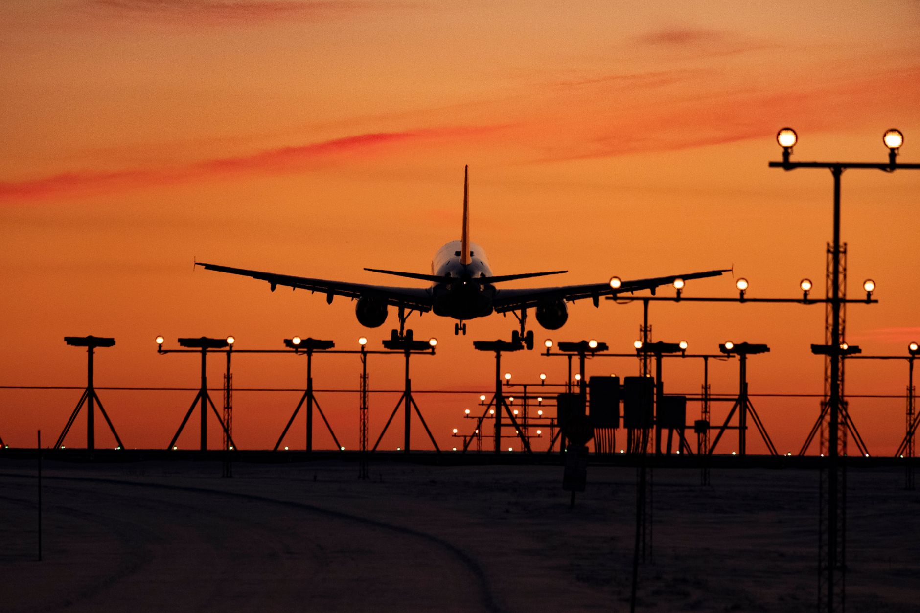 Une silhouette d'un avion atterrissant au coucher du soleil, capturant le ciel vif et les lumières de la piste.