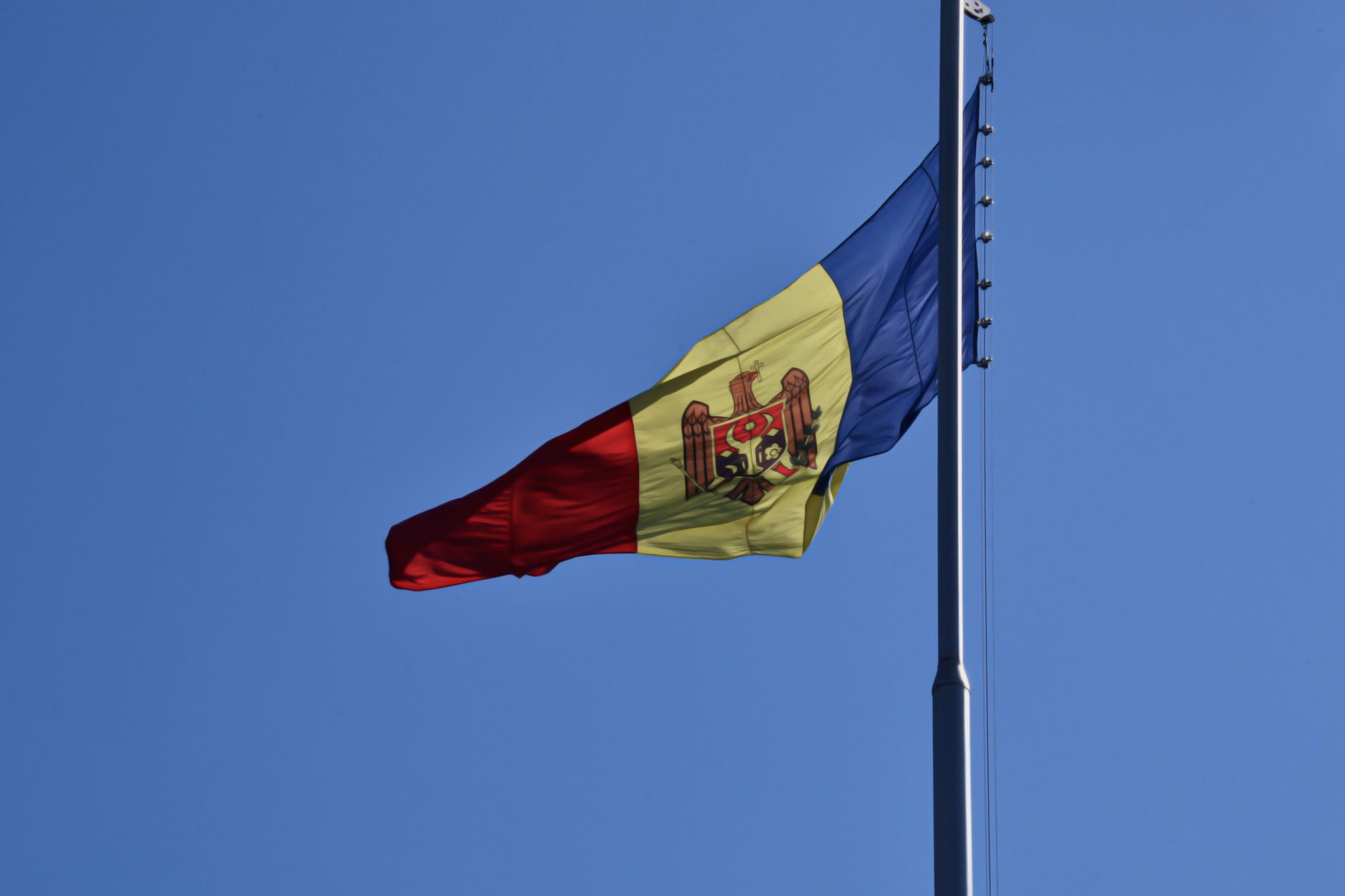 Le drapeau moldave flotte élégamment sur un mât sous un ciel bleu clair.